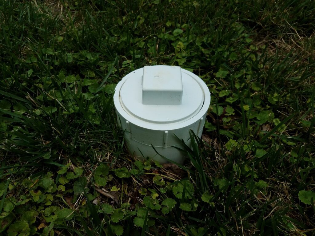 white plastic sewer clean out pipe in green grass