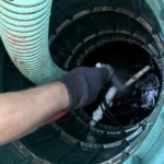Technician pumping a septic tank with a green hose inside the tank riser.