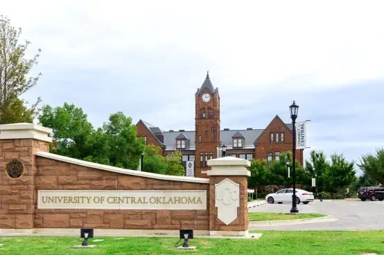 Old North Tower of University of Central Oklahoma in Edmond, OK | Cyclone Septic & Plumbing | Cyclone Septic & Plumbing Brick campus entrance sign reading 'University of Central Oklahoma' with a red brick clock-tower building and trees in the background.