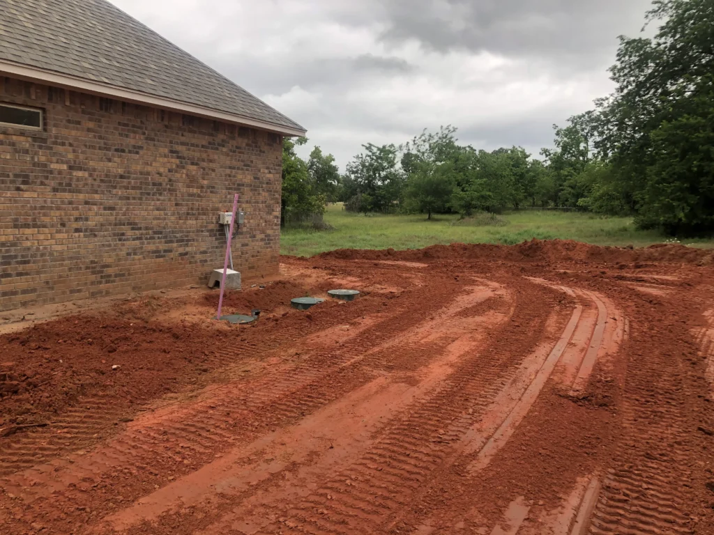 Septic system installation in Oklahoma red dirt beside a home