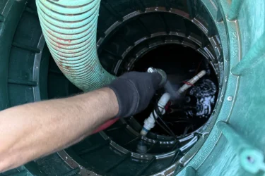 Technician pumping a septic tank with a green hose inside the tank riser.