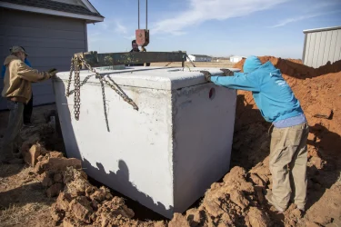 Workers guiding a large concrete septic tank into place during installation.