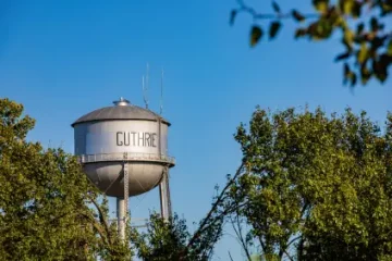 Water tower labeled 'GUTHRIE' peeking above trees against a bright blue sky.